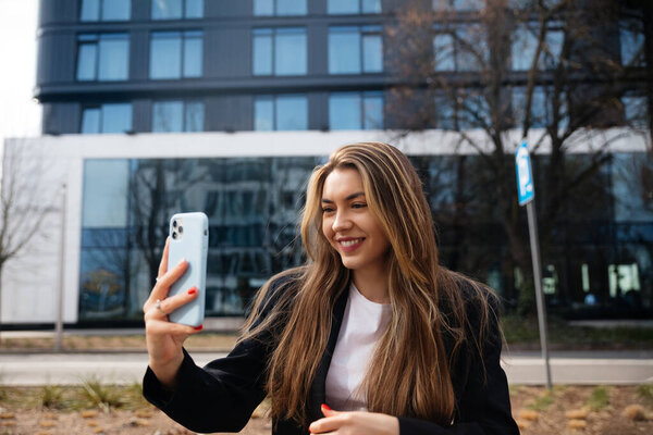 Young woman smiling while taking a selfie outdoors in a modern u