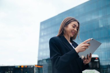 Professional woman engaged with a tablet in an urban environment, surrounded by modern architecture, highlighting technology and connectivity