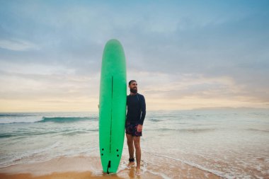 bearded man with surfboard standing near a beach. Man with surfing board outdoors on a summer day