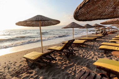 Beautiful sandy beach with parasols and sun loungers on the Turkish Aegean coast near Izmir and the Greek islands in the Mediterranean Sea in the evening sun in summer, Turkey Europe and Asia