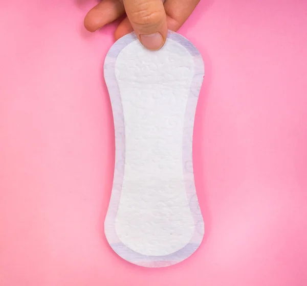 Woman is holding sanitary napkin in hand on pink background - menstrual hygiene concept