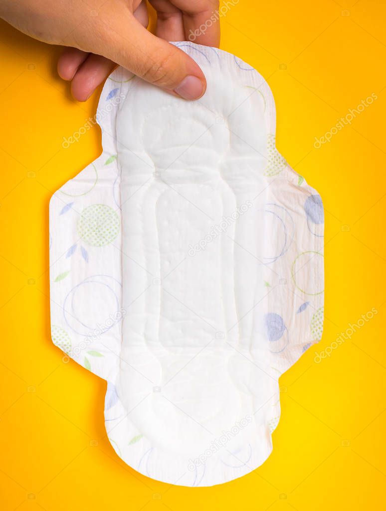 Woman is holding sanitary napkin in hand on yellow background - menstrual hygiene concept