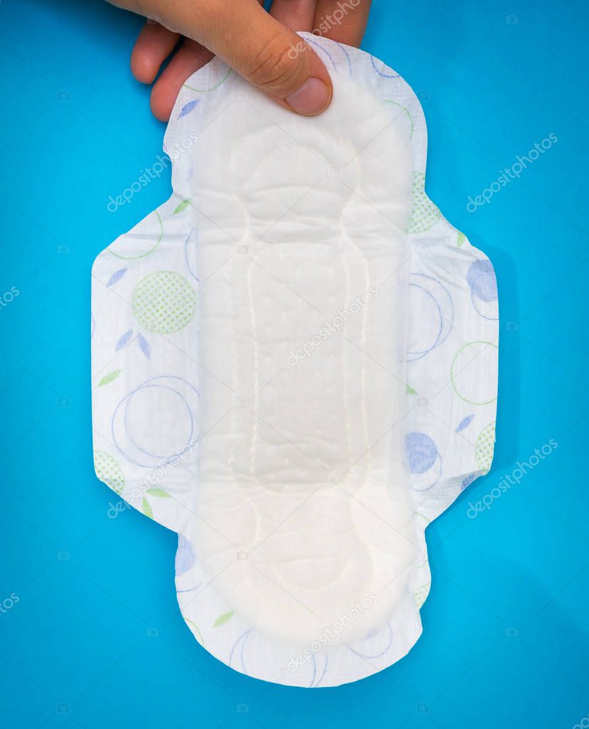 Woman is holding sanitary napkin in hand on blue background - menstrual hygiene concept