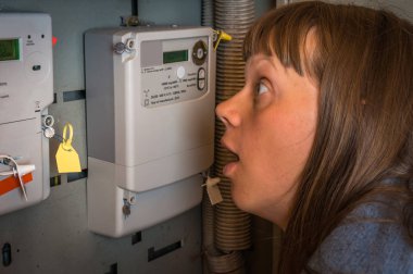 Terrified woman is checking electricity meter - consumption and expensive electricity concept clipart