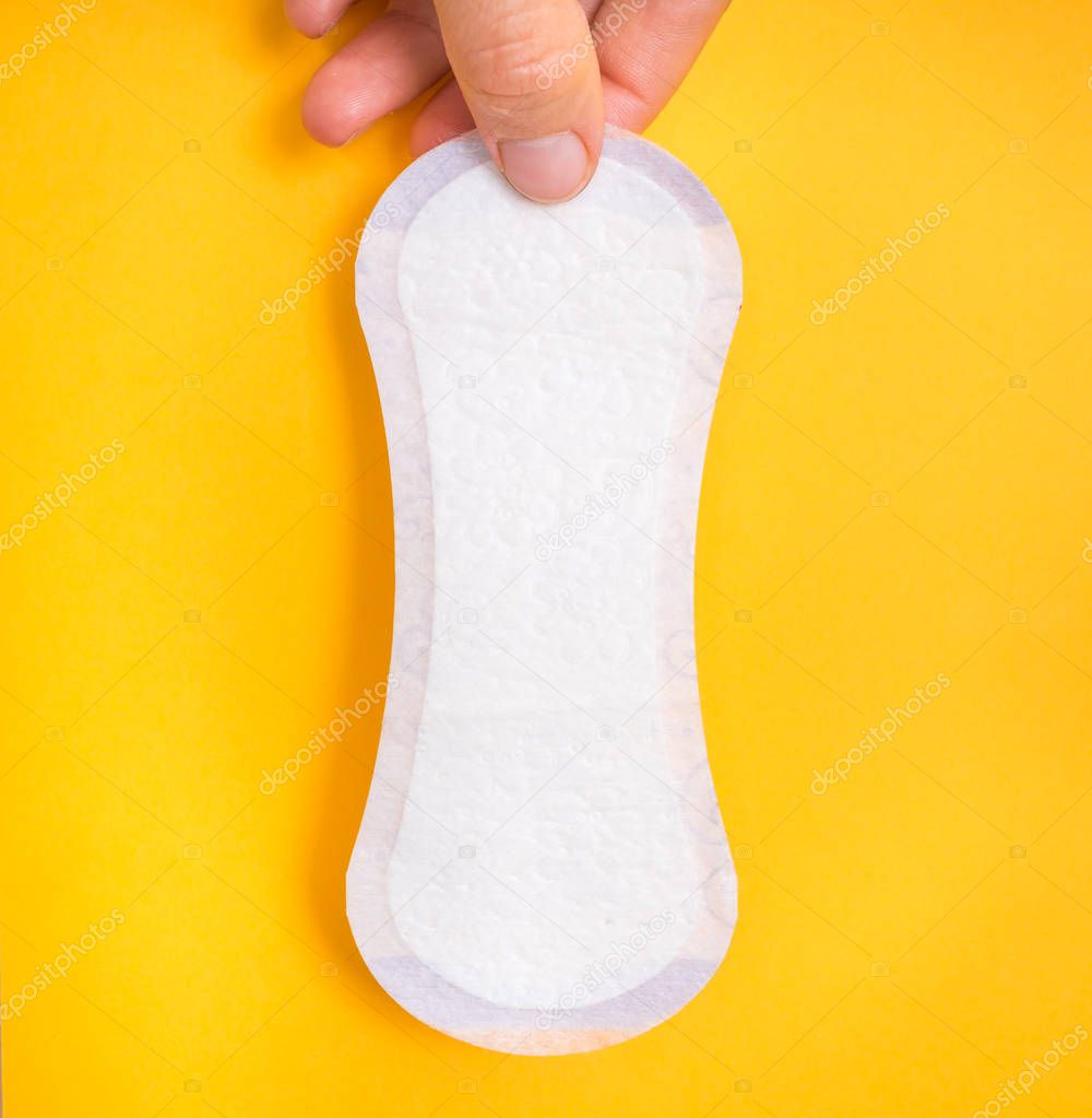 Woman is holding sanitary napkin in hand on yellow background - menstrual hygiene concept