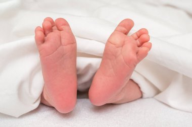 Yeni doğan bebek ayak beyaz battaniye altında yatakta