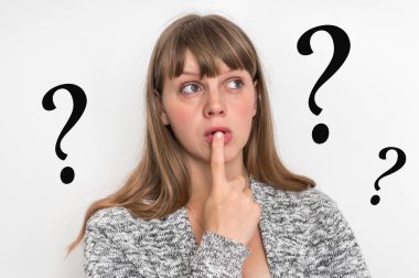 Dudaklarında parmak ve arka planda soru işaretleri olan düşünceli bir kadın.
