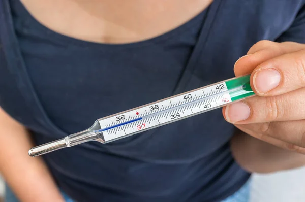 Woman with fever is holding mercury thermometer - cold and flu concept