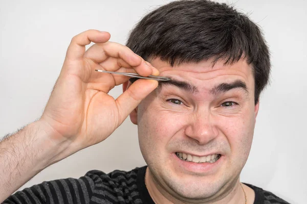 Young man is plucking eyebrows with tweezers