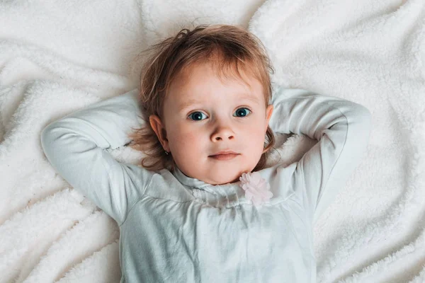 Smiling child is lying on back on white blanket — Stock Photo, Image