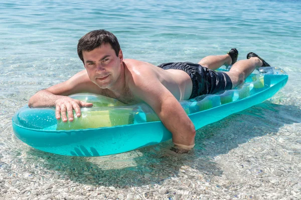 Sonríe hombre sexy nada en el mar con colchón inflable — Foto de Stock