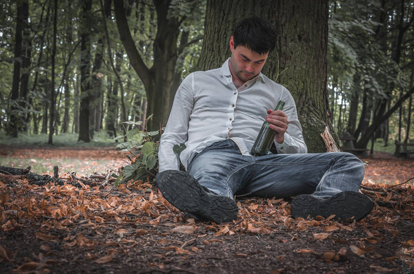 Пьяный лежит на земле под деревом с пивной бутылкой.
