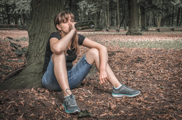 Женщина пьет вино в парке и сидит под деревом
