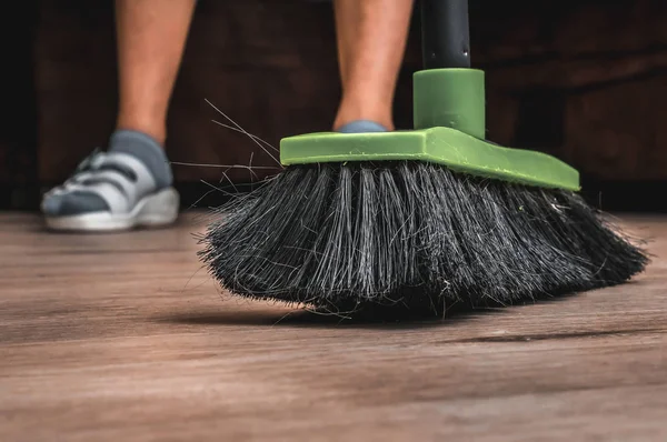 Woman with broom sweeping wooden laminate floor