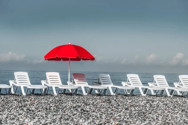 Plastic deck chairs and red umbrella on the beach