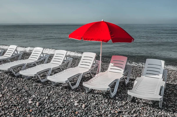 Plastic deck chairs and red umbrella on the beach