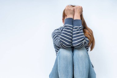 Üzgün ve depresif kız gri arka planda izole edilmiş. O yalnız ve ellerini yüzünü kapatarak oturuyor..