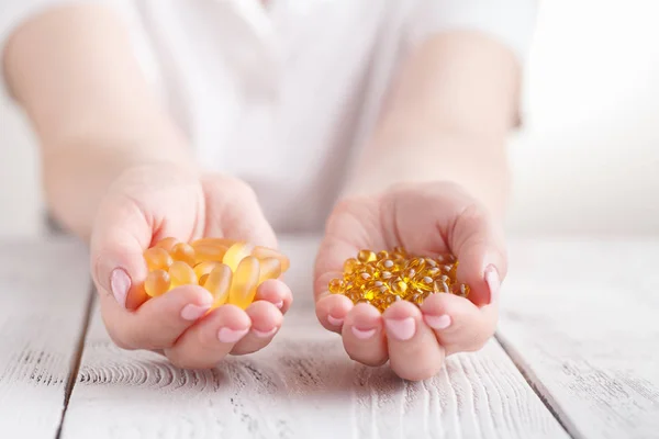 medicine, nutritional supplements and people concept - close up of hands holding cod liver oil capsules