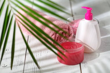 Kozmetik şişe kapları ile yeşil bitki yaprakları üzerinde beyaz ahşap masa