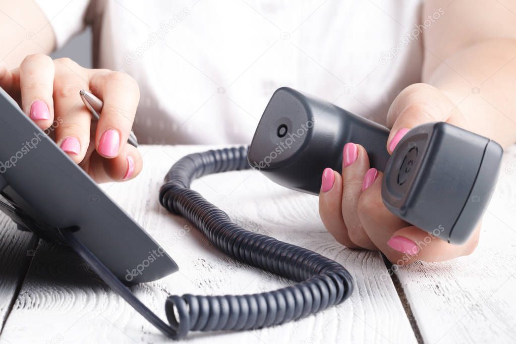 Female hand holding phone receiver and dialing number