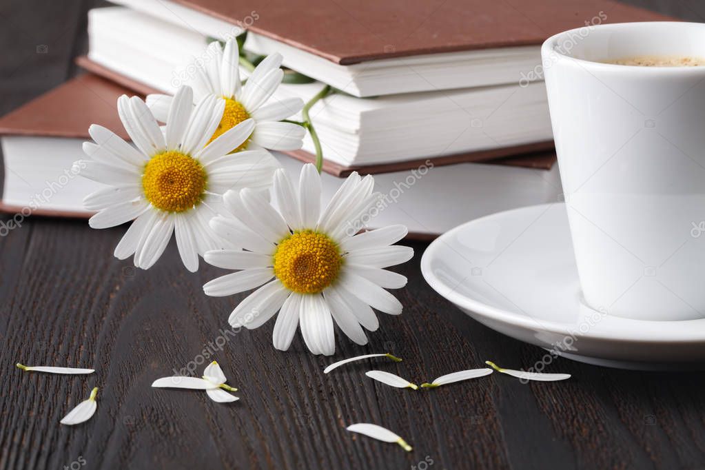 Cup of coffee, chamomile and a book on the wooden table