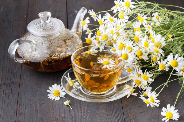 Glass teapot and cup with green tea on old wooden table with fresh herbs
