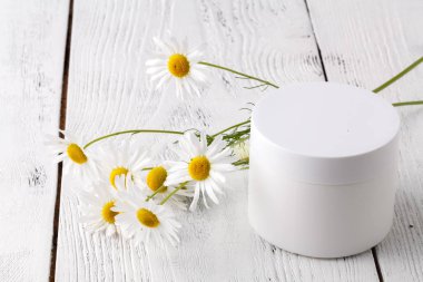 Plastik Konteyner ile hafif bir arka plan üzerinde krem ve papatya çiçek açtı. Bitkisel Dermatoloji kozmetik hijyenik krem. Doğal güzellik ürünü