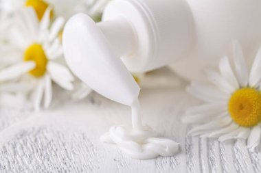 Plastik Konteyner ile hafif bir arka plan üzerinde krem ve papatya çiçek açtı. Bitkisel Dermatoloji kozmetik hijyenik krem. Doğal güzellik ürünü