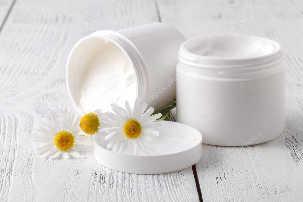 Opened plastic container with cream and chamomile flower on a light background. Herbal dermatology cosmetic hygienic cream. Natural beauty product