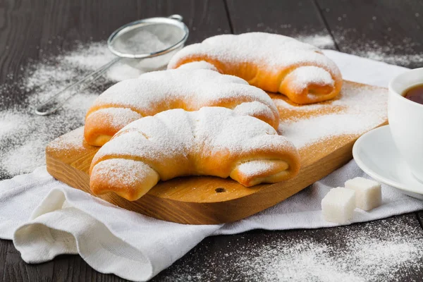 Biscuit rolls filled with jam with powdered sugar on top on plate over wooden table — Stock Photo, Image