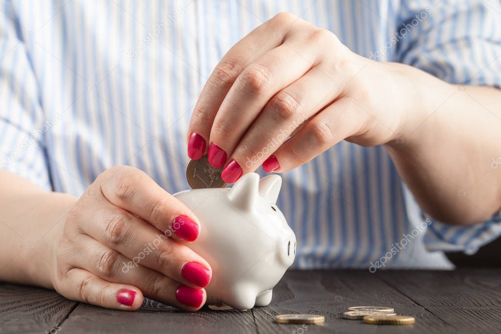 Close-Up Woman Hand is Putting a Money Coin into Piggy Bank on table