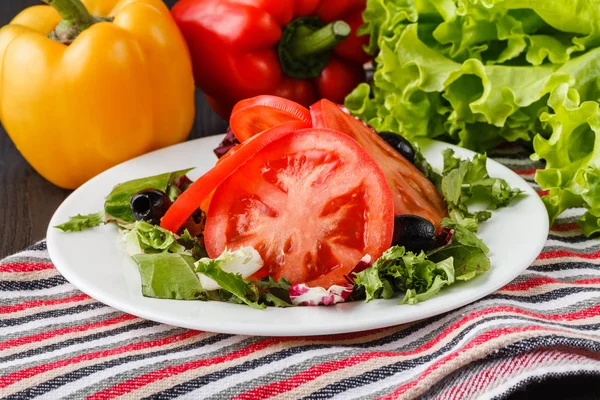 Летний салат с помидорами в белой тарелке на деревянном столе — стоковое фото