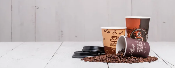 Kávová zrnka s papírovým šálkem na dřevěné pozadí — Stock fotografie