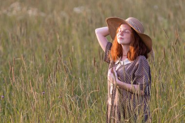 Kızıl saçlı manken gün batımında çayırda poz veriyor.