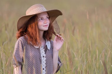 Şık bir elbiseyle gün batımında çayırda poz veren kızıl saçlı kız.