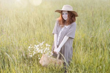 Duygusal kızıl kız, yaz otlağında, gün batımında zarif bir elbiseyle oynuyor.