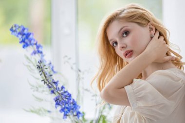 Harika gülüşü ve romantik saç stili olan neşeli, sevimli kız beyaz odada zevkle poz veriyor. Güneşli bir sabahta çiçekli güzel bir genç kadının portresi.