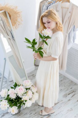 Beyaz ve gül rengi şakayıklar tutan güzel bir kızın kapalı çekimleri. Büyük buketli, çiçeklerinin tadını çıkaran bir kadın.