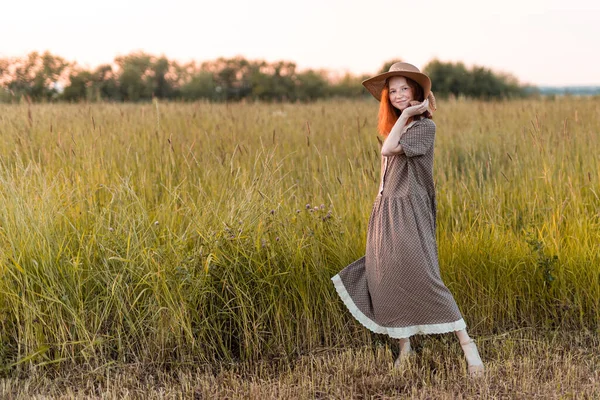 赤い頭の女の子がエレガントなドレスで日没時に夏の牧草地にポーズをとって — ストック写真