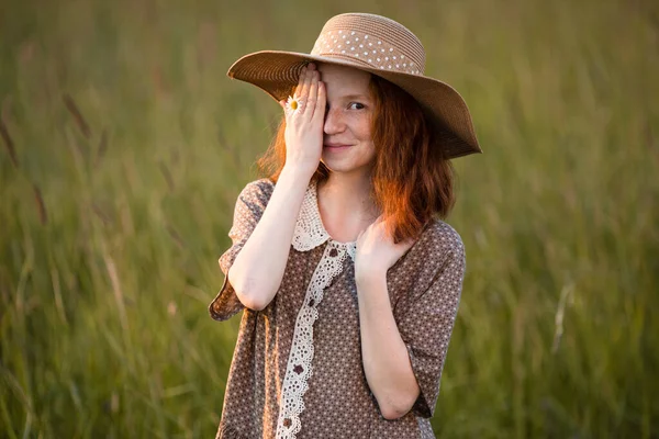 赤い頭の女の子がエレガントなドレスで日没時に夏の牧草地にポーズをとって — ストック写真