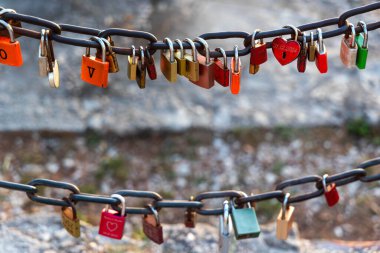 Metal zincirde asılı renkli asma kilitler. Aşkı ve bağlılığı sembolize eden çeşitli renkli asma kilitler, romantik bir geleneğin bir parçası olarak açık havada metal bir zincirde asılı duruyor.