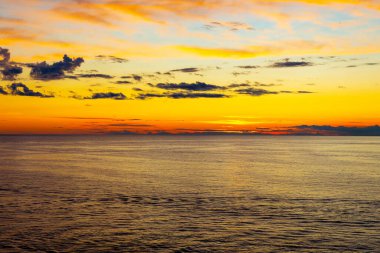 Canlı gökyüzü renkleriyle altın okyanus gün batımı. Gün batımında sakin deniz manzarası. Parlayan altın bir gökyüzü, hafif dalgalar ve dağınık bulutlar. Huzurlu, rüya gibi bir atmosfer yaratıyor.