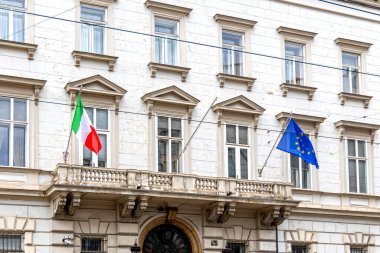Tarihi bina cephesinde İtalyan ve AB bayrakları. İtalyan ve Avrupa Birliği bayrakları klasik bir Avrupa hükümet binası veya büyükelçilik binasının dışında mimari ayrıntılarla asılı