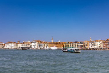 Venedik, İtalya, 11 Ağustos 2025: güneşli bir günde Venedik kıyısı. Venedik rıhtımının manzarası Büyük Kanal 'daki tarihi binalar ve tekneler berrak mavi gökyüzünün altında..