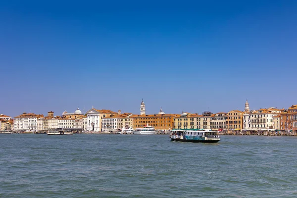Venedik, İtalya, 11 Ağustos 2025: güneşli bir günde Venedik kıyısı. Venedik rıhtımının manzarası Büyük Kanal 'daki tarihi binalar ve tekneler berrak mavi gökyüzünün altında..