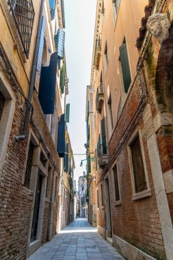 Venedik 'te açık panjurlu dar kaldırım taşı caddesi. Venedik 'te tuğla binalar, açık ahşap panjurlar, balkonlar ve sokakları aydınlatan hafif ışık ile büyüleyici dar bir cadde.