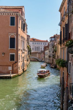 Venedik, İtalya, 11 Ağustos 2025: güneşli bir günde Venedik 'te dar kanallarda gezinen tekneler. Su taksileri ve botlar Venedik 'te güneşli bir kanal boyunca seyahat ediyor. Tarihi binalar ve çiçeklerle dolu balkonlarla dolu..