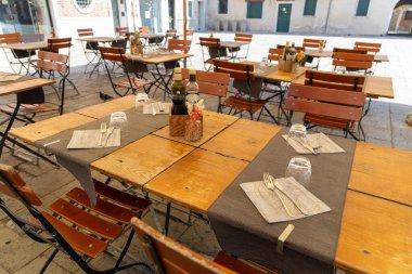 Güneşli meydanda boş restoran masaları. Güneşli bir günde müşteriler için sakin bir Avrupa meydanındaki açık bir restorana ahşap masalar ve sandalyeler yerleştirin.