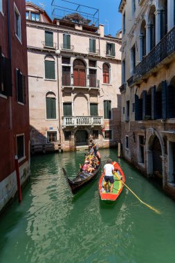 Venedik, İtalya, 11 Ağustos 2025 Dar Venedik kanalında Gondol ve kayık. Turistler gondola binerken bir adam güneşli bir günde tarihi Venedik binaları arasındaki dar bir kanalda renkli bir tekneye kürek çekiyor..