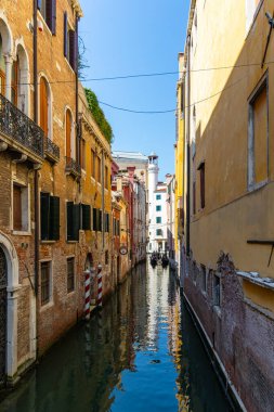 Venedik, İtalya, 11 Ağustos 2025, uzak gondollu renkli Venedik kanalı. Venedik 'teki dar bir kanal, berrak mavi gökyüzünün altındaki gondolları gösteren canlı eski binalarla dolu..